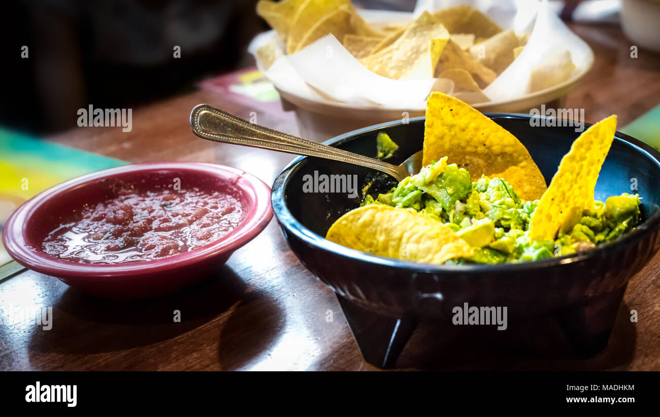 Eine Schüssel mit Guacamole mit Salsa und Chips im Hintergrund. Stockfoto