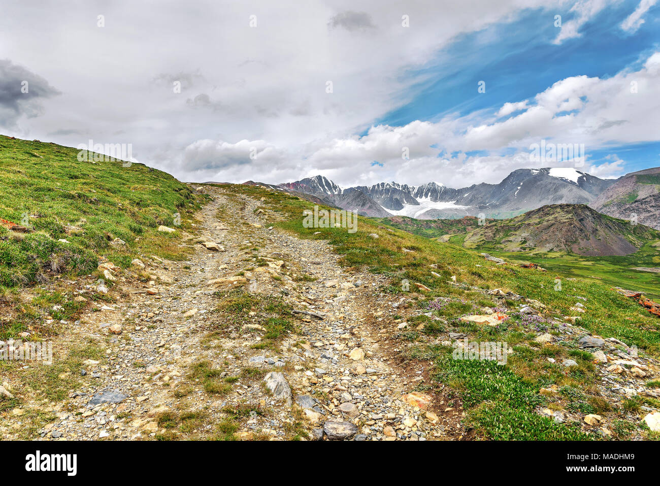 Rocky steile Straße hoch oben in den Bergen, grünen Gras und Gletscher auf dem Hintergrund der blauen Himmel und Wolken Stockfoto