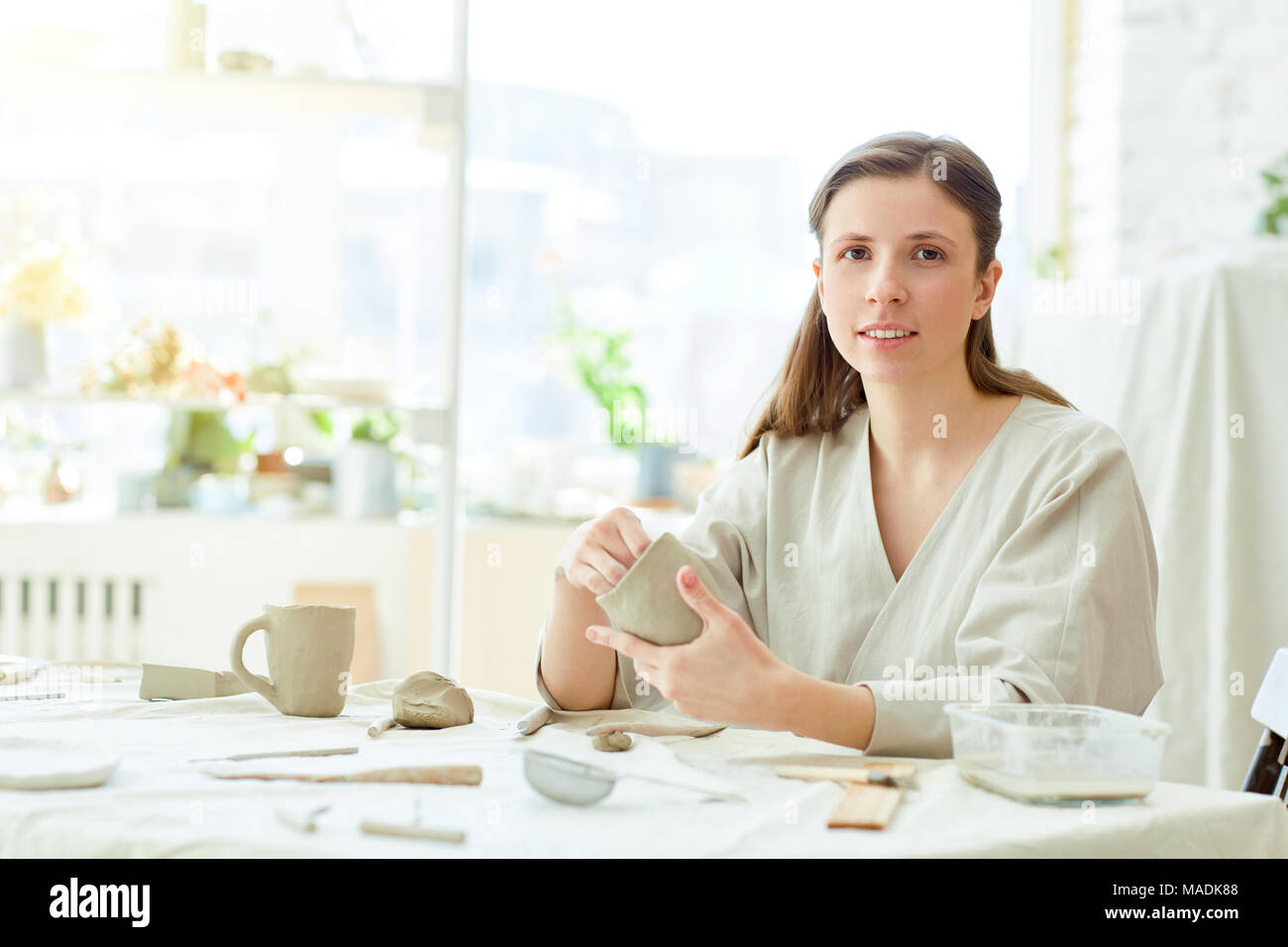 Kreative weiblichen Blick auf Kamera von Ihrem Arbeitsplatz, während sie Tassen und andere handgefertigte Produkte Stockfoto