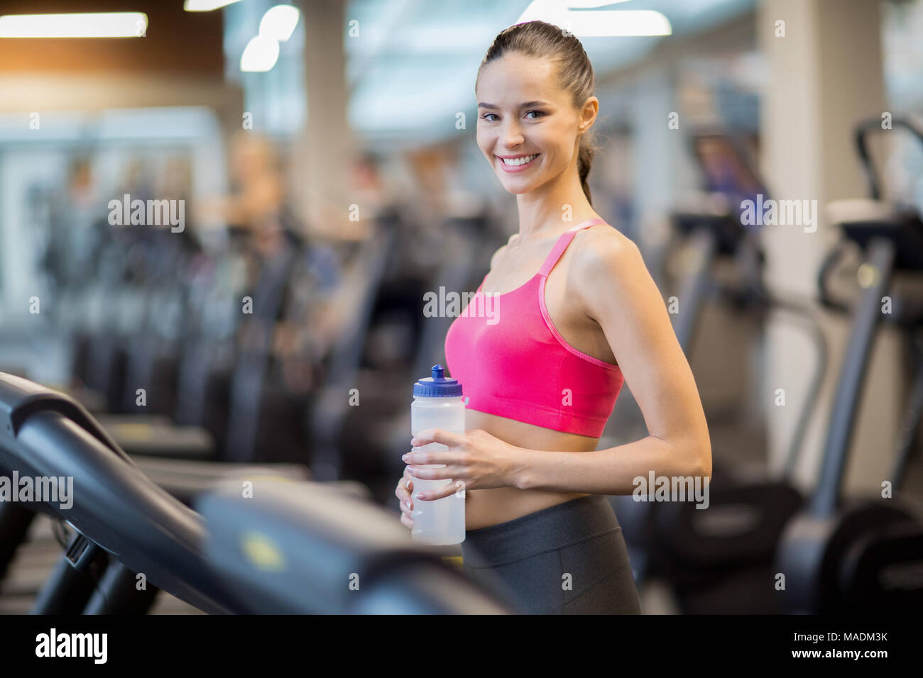 Glückliche junge Sportlerin mit Kunststoff Flasche Wasser auf Kamera im modernen Fitnessraum oder Sport Center Stockfoto