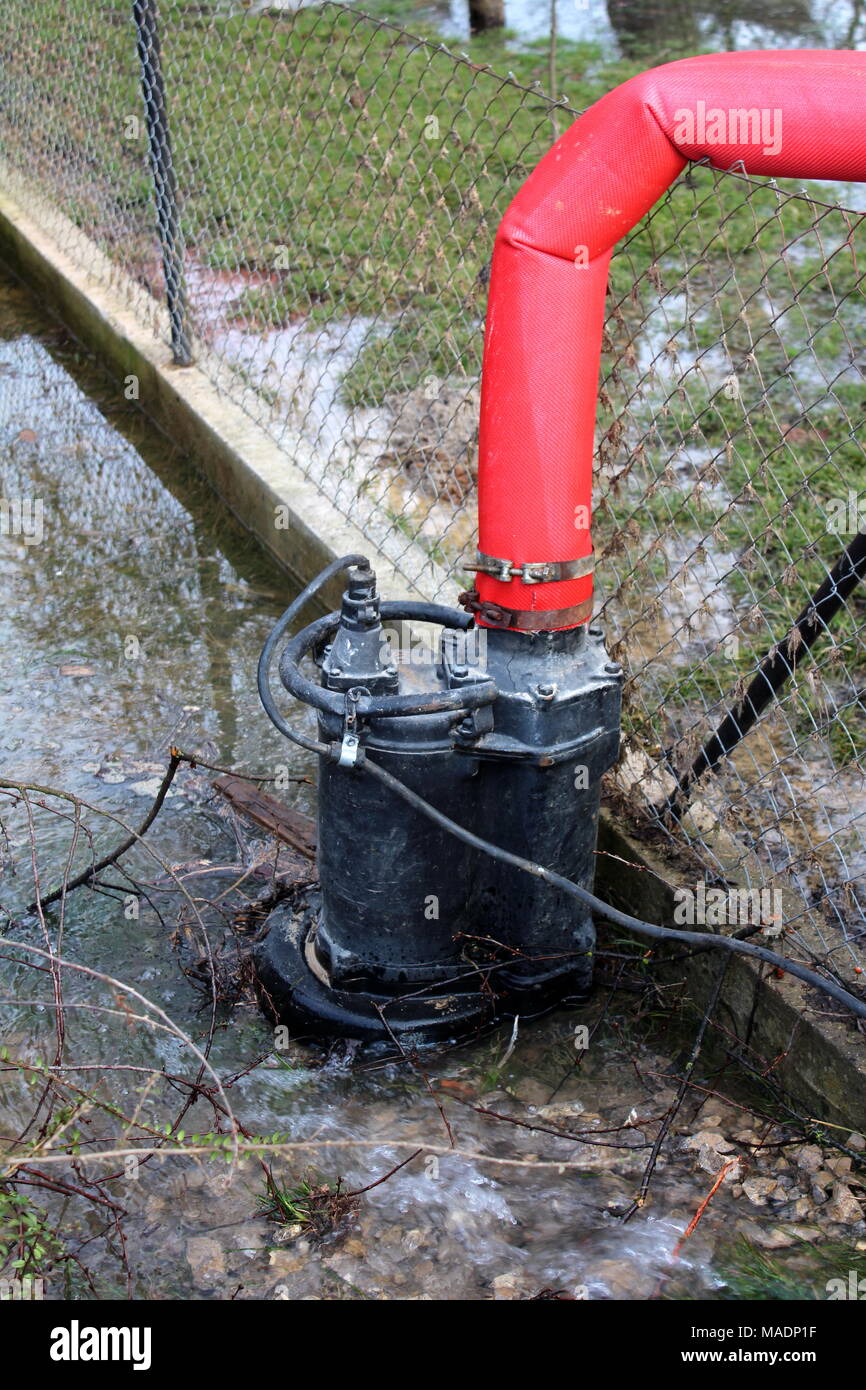 Wasserpumpe Pumpen von Wasser aus dem Garten während der Flut durch die  großen roten Schlauch über draht zaun Stockfotografie - Alamy