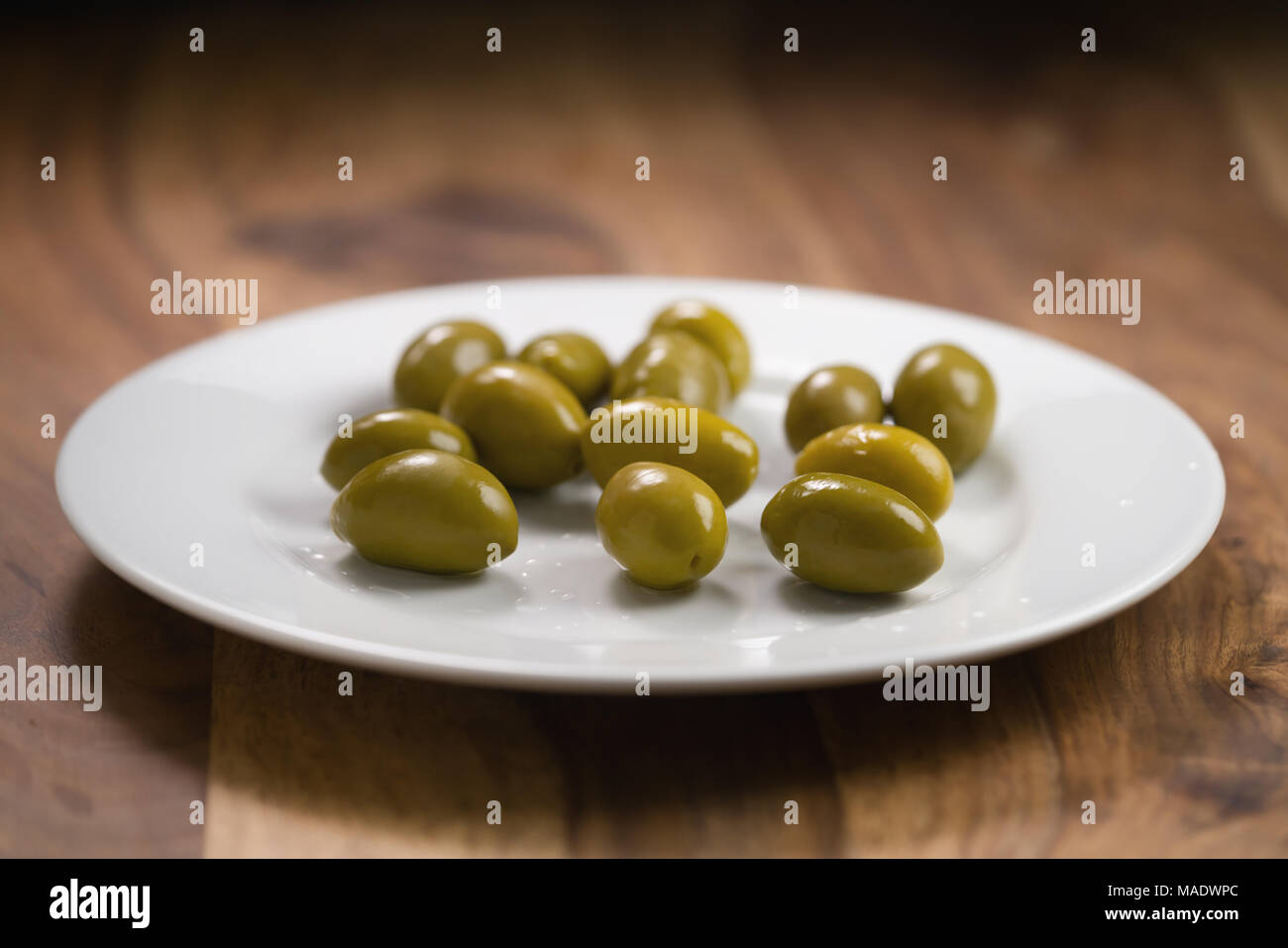Große grüne gesalzene Oliven auf weiße Platte auf Holztisch, flacher Fokus Stockfoto