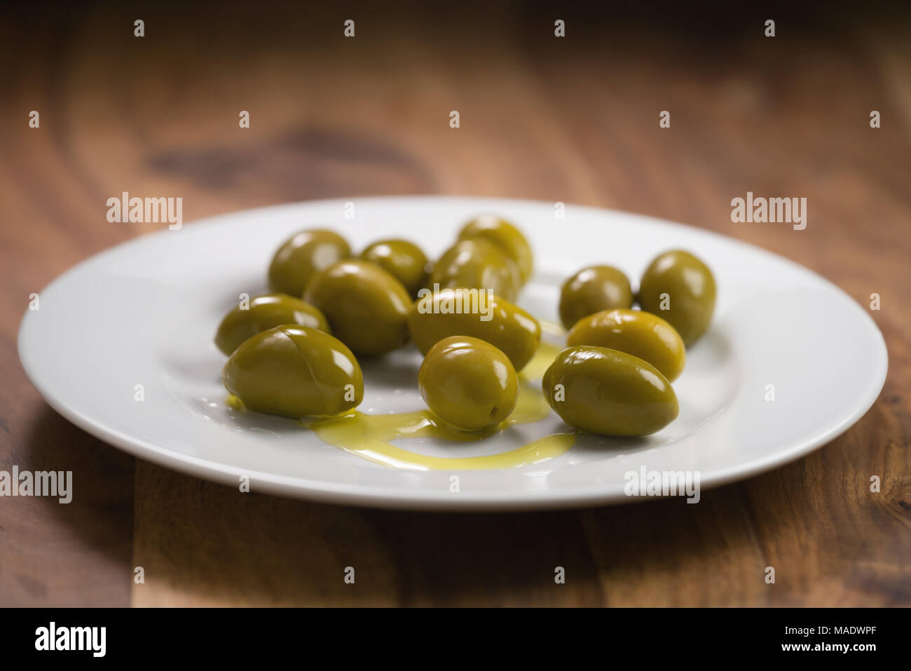 Große grüne gesalzene Oliven auf weiße Platte auf Holztisch, flacher Fokus Stockfoto