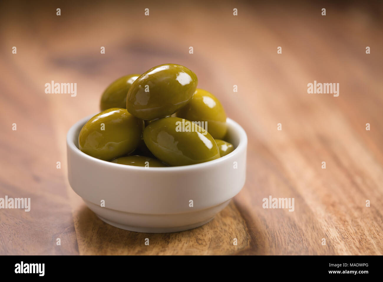 Große grüne gesalzene Oliven in Weiß Schüssel auf Holztisch, flacher Fokus Stockfoto