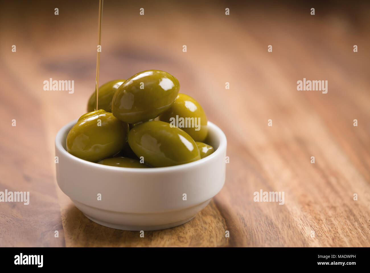 Große grüne gesalzene Oliven in Weiß Schüssel auf Holztisch, flacher Fokus Stockfoto