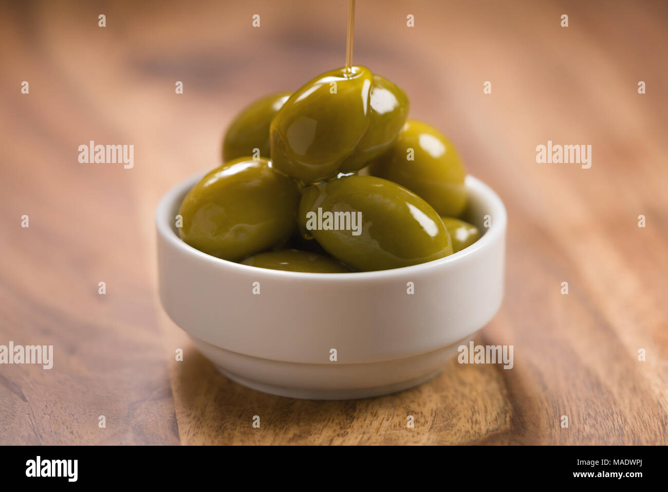 Große grüne gesalzene Oliven in Weiß Schüssel auf Holztisch, flacher Fokus Stockfoto
