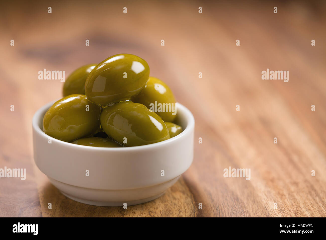Große grüne gesalzene Oliven in Weiß Schüssel auf Holztisch, flacher Fokus Stockfoto