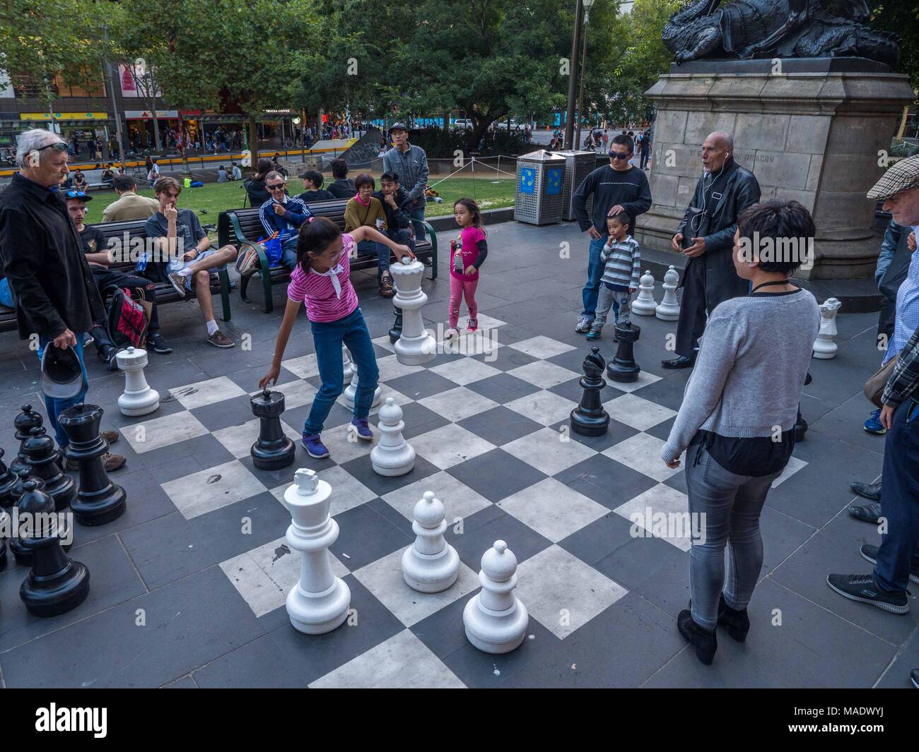 Jungen asiatischen Mädchen und älteren Mann spielt Schach im Freien vor der Bibliothek. Junge Mädchen, die Schachfiguren. Alte Männer streiten sich bewegt. Stockfoto