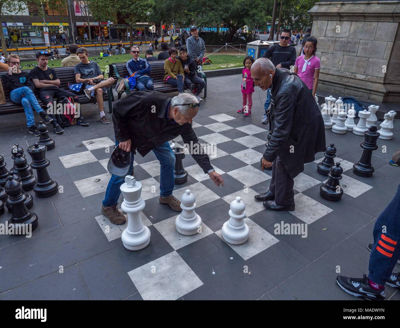 Jungen asiatischen Mädchen und älteren Mann spielt Schach im Freien vor der Bibliothek. Junge Mädchen, die Schachfiguren. Alte Männer streiten sich bewegt. Stockfoto