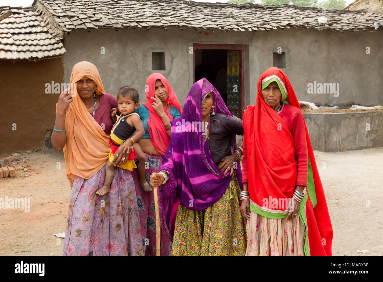 Vier Frauen mit abgedeckten Köpfe tragen Bunte Saris und ein Kind außerhalb Lehmhütten in einem Dorf in der Nähe von Shahpura, Rajasthan, Indien. Stockfoto
