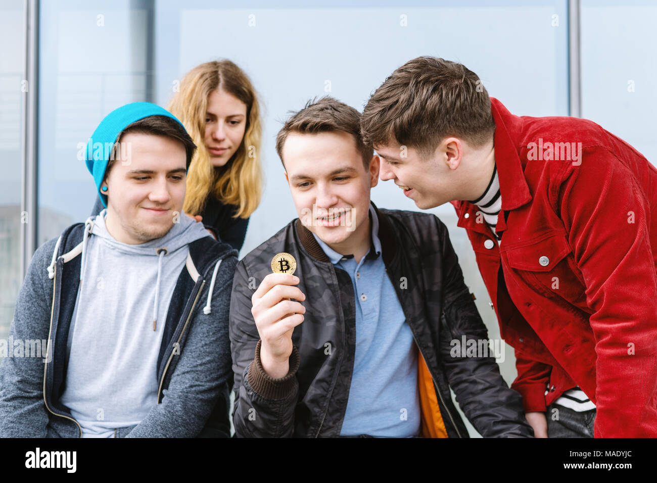 Junger Mann mit bitcoin Münze zu seinem Intrigierte Gruppe von Freunden Stockfoto