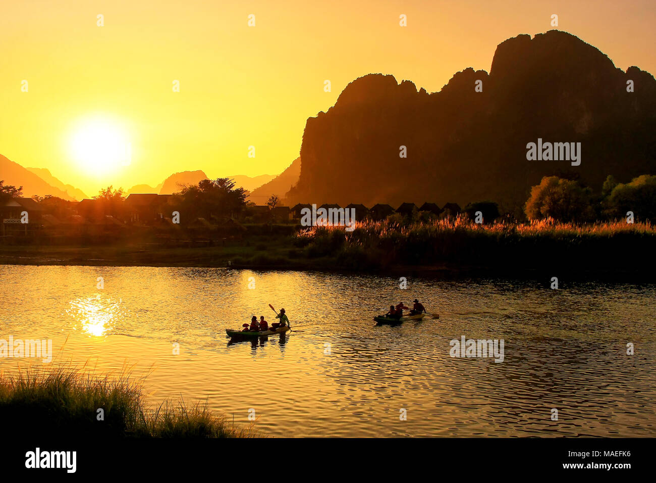 Nam Song Fluss bei Sonnenuntergang mit Silhouettiert Felsformationen und Kajakfahrer in Vang Vieng, Laos. Vang Vieng ist ein beliebtes Reiseziel für Abenteuer Tourismus Stockfoto