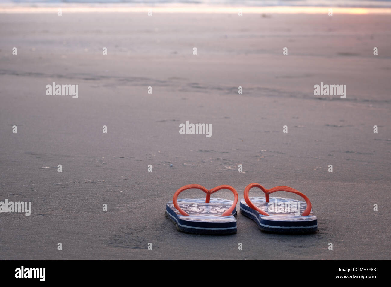 Orange Beach Sandalen an der sandigen Küste bei Sonnenuntergang. Stockfoto