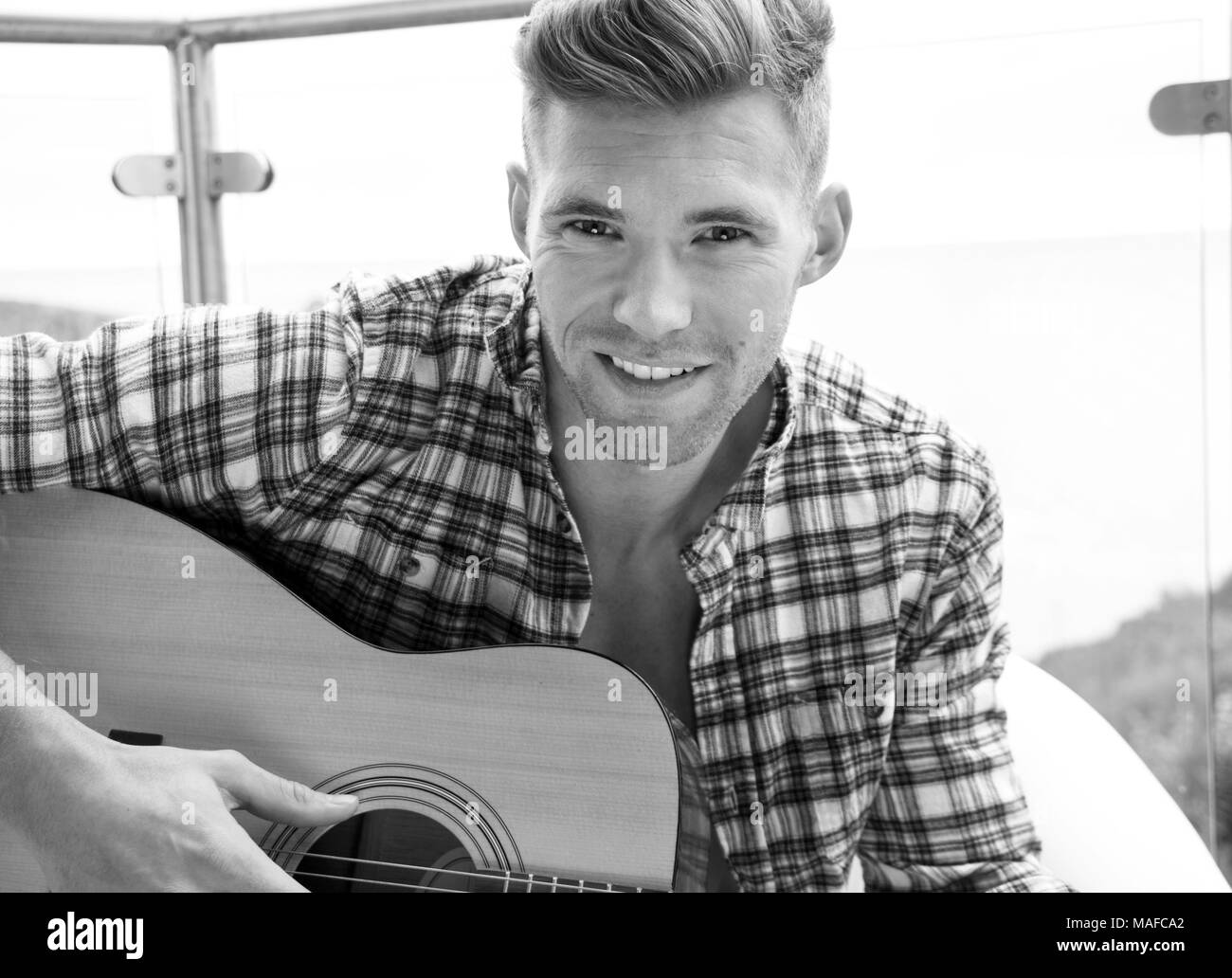 Stattliche Musiker Gitarre Spielen auf Hotel Balkon mit Blick auf das Meer im Hintergrund. Stockfoto
