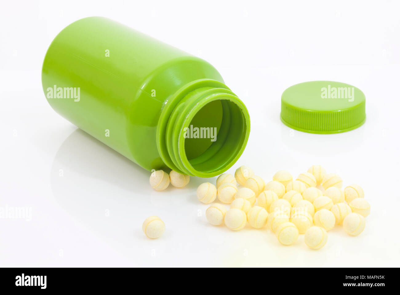 Runde gelbe probiotische Tabletten Verschütten von grün Medikation Flasche gegen den weißen Hintergrund. Stockfoto