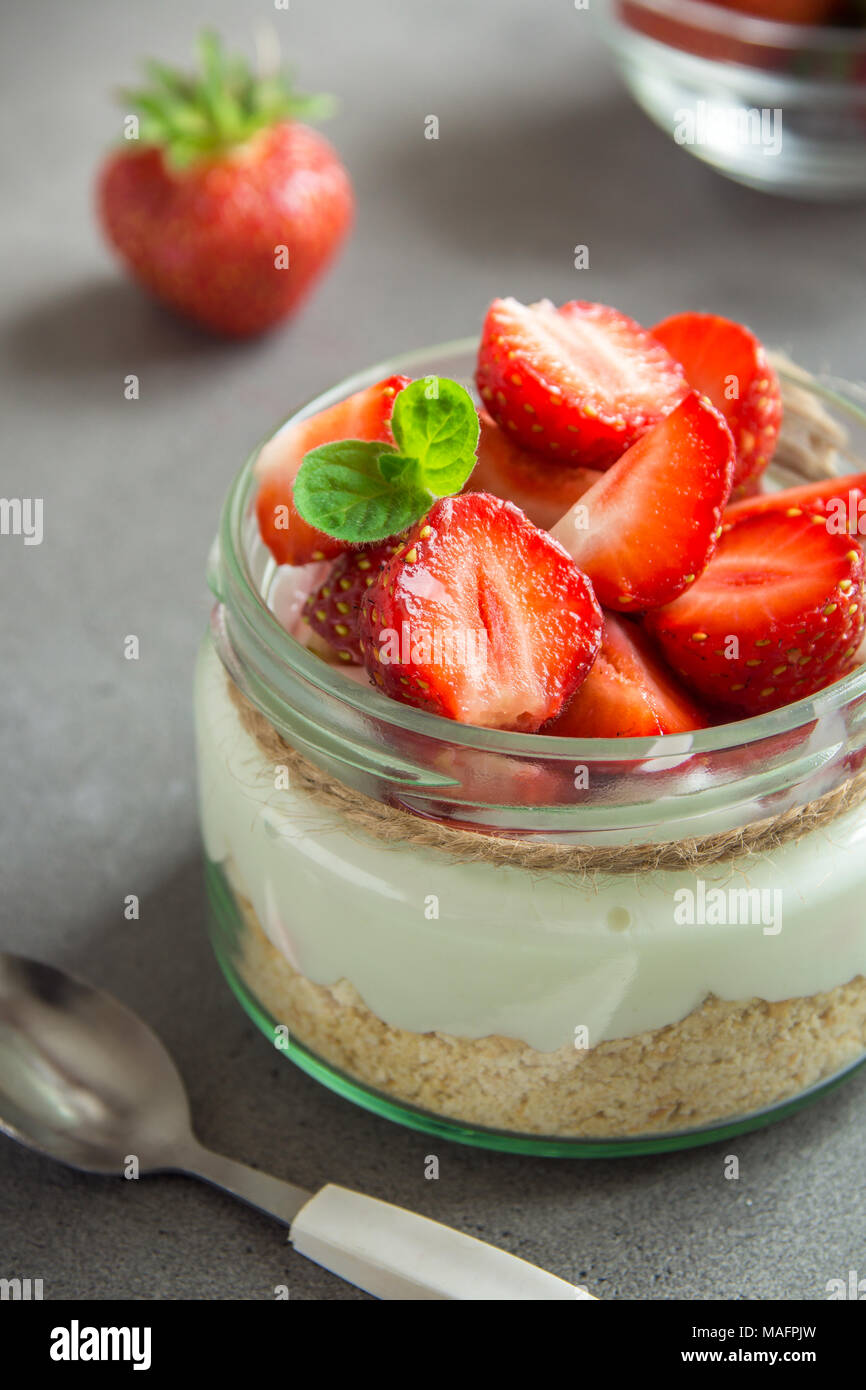 Strawberry cheesecake in Glas Glas mit frischen Erdbeeren und Sahne Käse auf grauem Beton Hintergrund. Gesunde hausgemachte Bio Dessert. Stockfoto