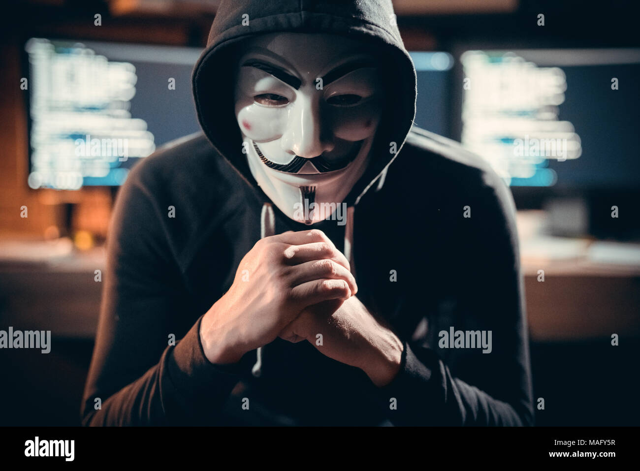 Junger Mann finanzielle Hacker im Büro sitzen tragen vendetta Maske suchen Kamera gefährlich Stockfoto