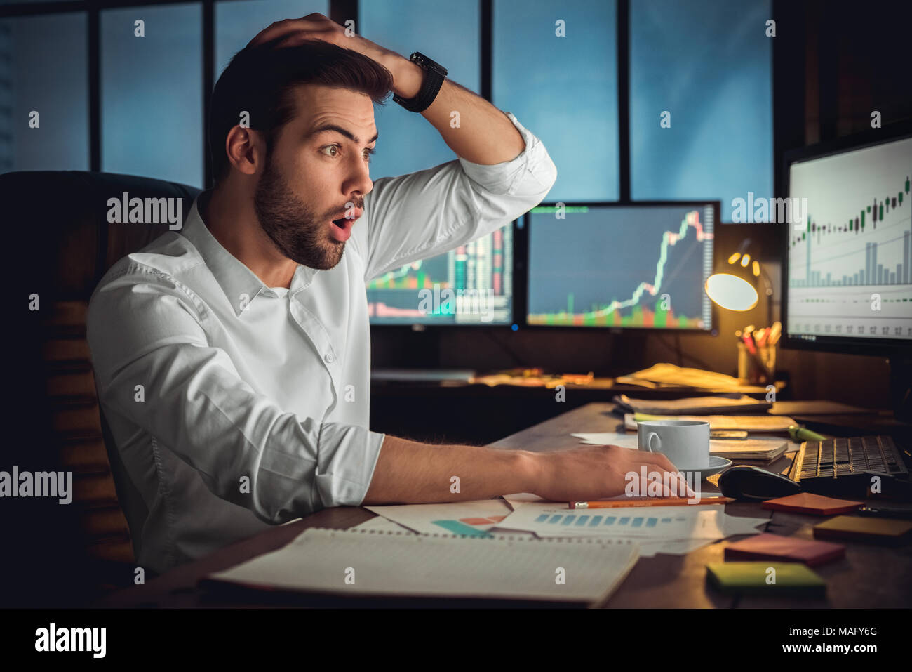 Junger bärtiger Mann Händler im Büro am Tisch sitzen auf dem Bildschirm berühren Haar schockiert Stockfoto