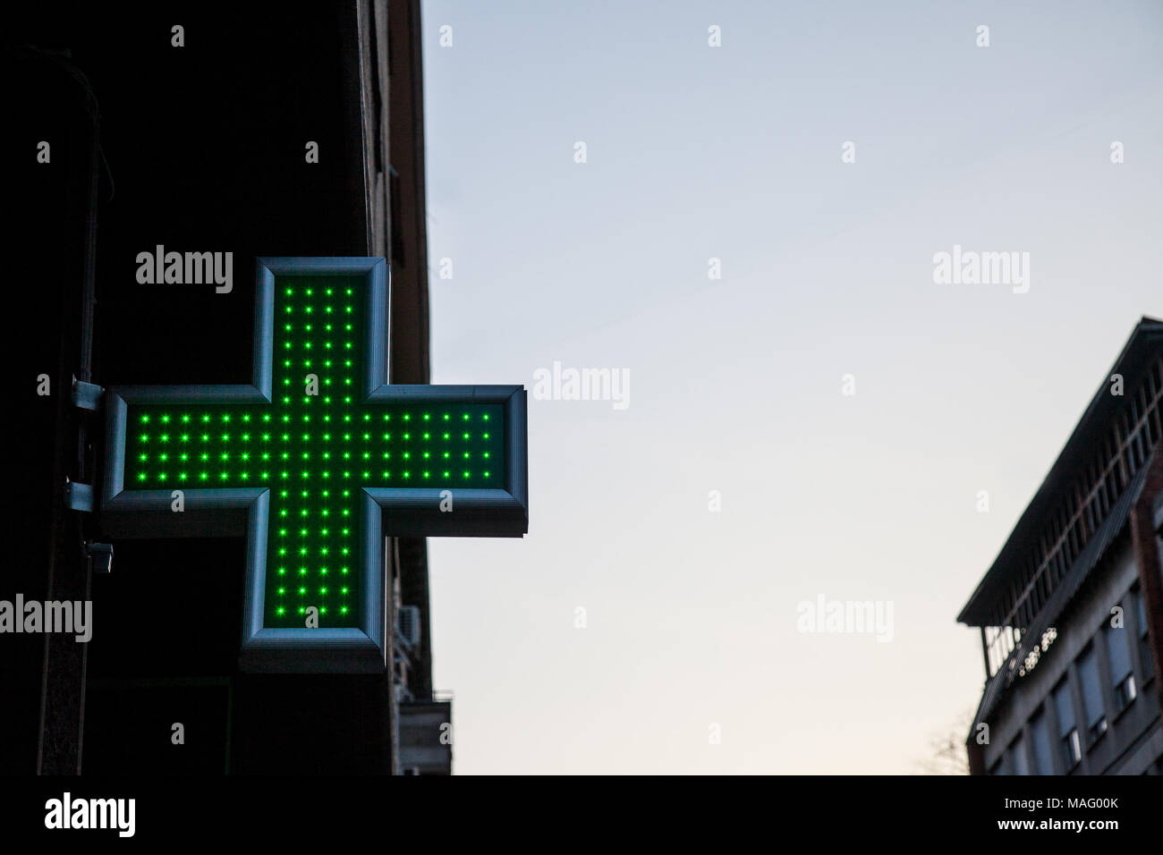 Apotheke Green Cross beleuchtet mit Neon und LED-Leuchten in den Sonnenuntergang. Dieses Kreuz ist ein universelles Symbol für Apotheke in Europa Bild von einem grünen Kreuz Anzeige Stockfoto