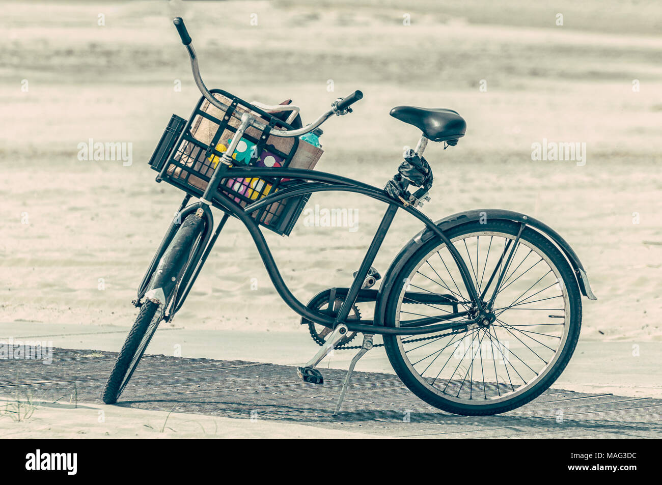 Ein altes Fahrrad mit einem Korb voller Sachen am Strand geparkt Stockfoto