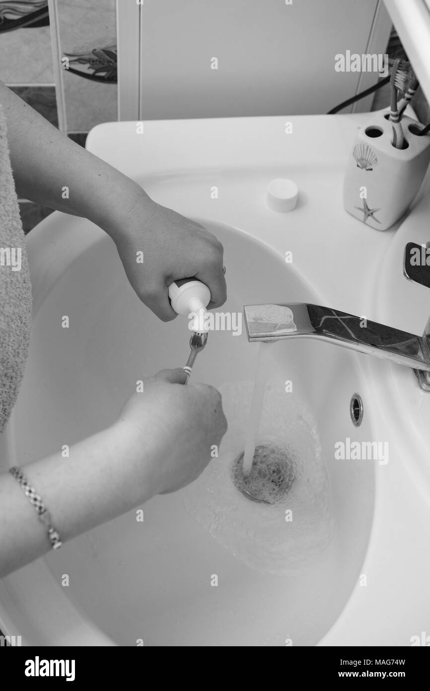 Schwarz-weiß Foto. Nahaufnahme der Hand einer jungen Frau quetschen Zahnpasta aus der Tube im Bad. Stockfoto