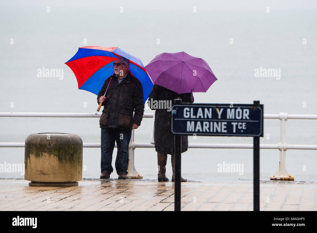 Aberystwyth Wales UK, Montag, 2. April 2018 britische Bank Urlaub Wetter: Menschen Schutz unter ihren Schirmen, wie Sie entlang der Promenade im strömenden Regen auf eine miserable und nasse Ostern Montag Feiertag in Aberystwyth Spaziergang auf der West Wales Küste Foto © Keith Morris/Alamy leben Nachrichten Stockfoto