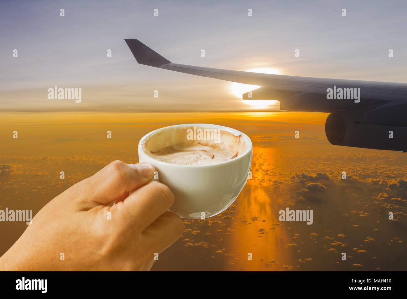 Tasse Kaffee in der Hand auf Wing's Flugzeug gegen goldenes Sonnenlicht am frühen Morgen Hintergrund Stockfoto