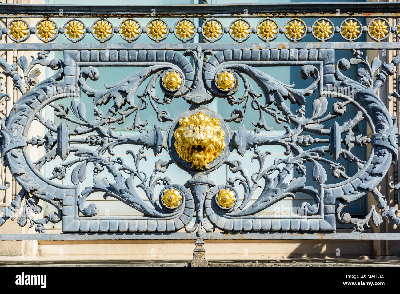 Nahaufnahme der schmiedeeisernen Geländer des Balkons Pariser Gebäude mit einem Golden Lion's Head in der Mitte durch pflanzliche umgeben dekoriert Stockfoto