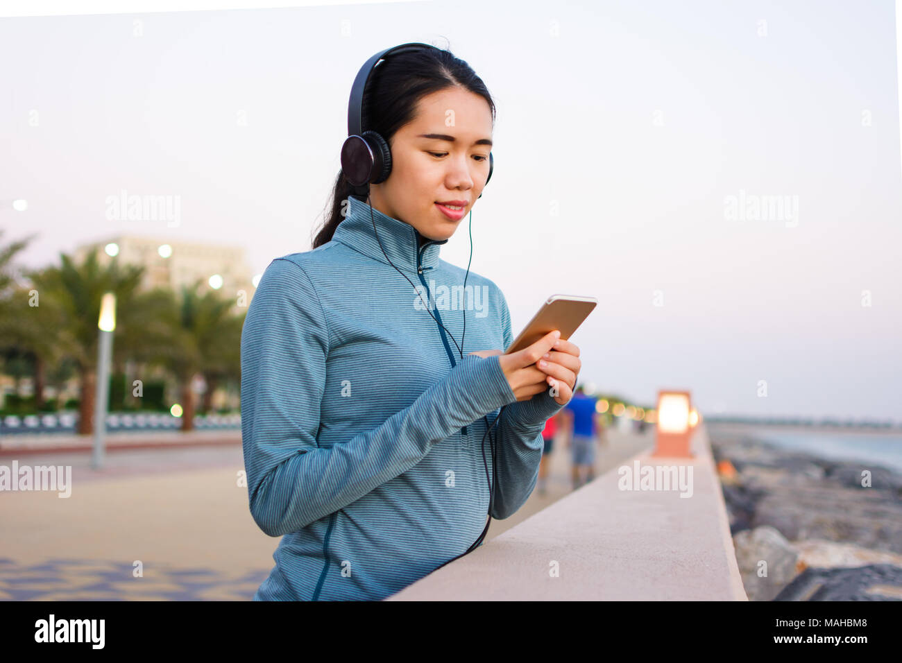Mädchen mit Telefon und Musik hören mit Kopfhörern auf dem Boardwalk Stockfoto