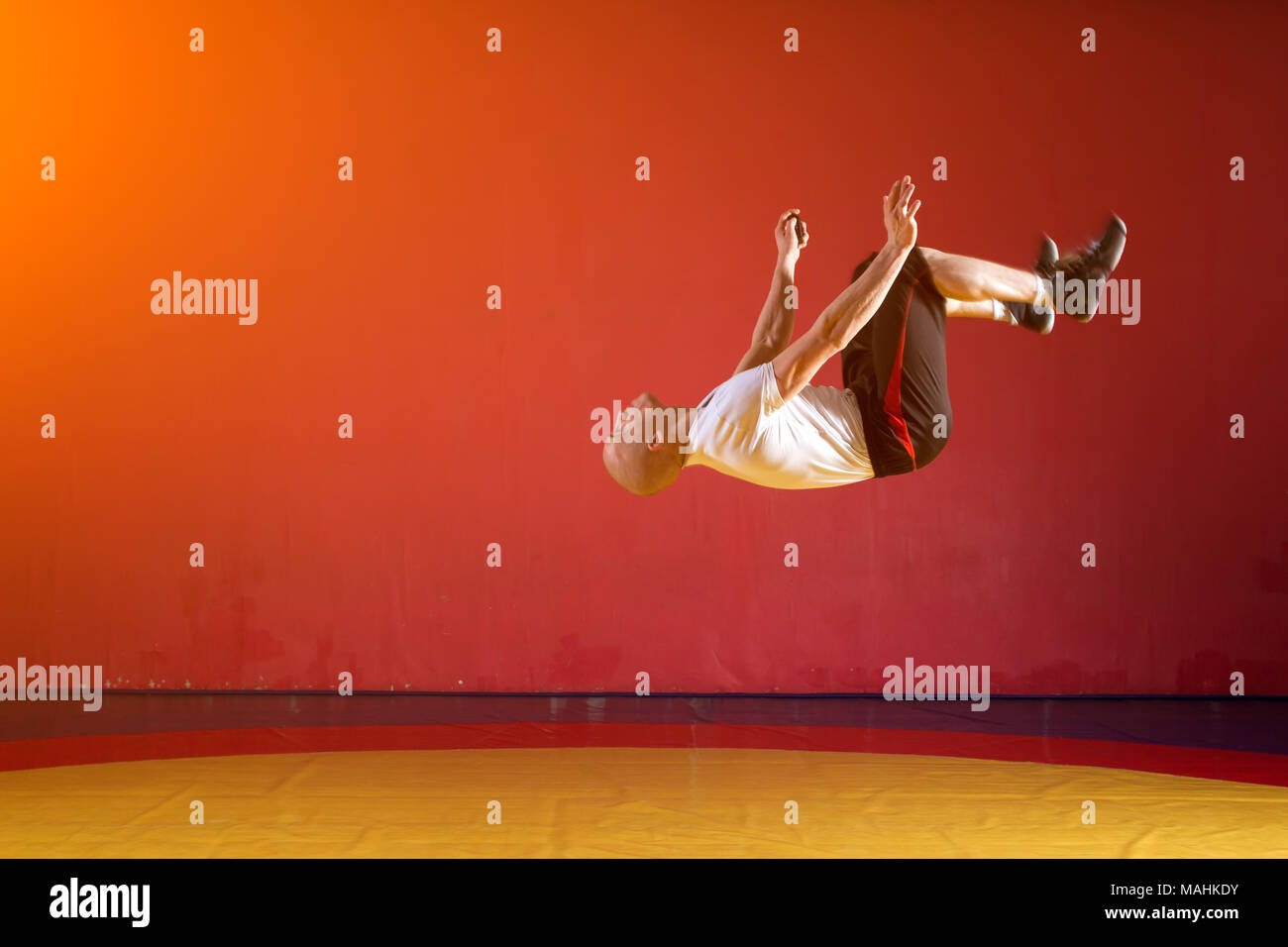 Ein junger sportlicher Mann in Sportkleidung macht einen Salto in der wrestling Hall. Parkour in der Turnhalle Stockfoto