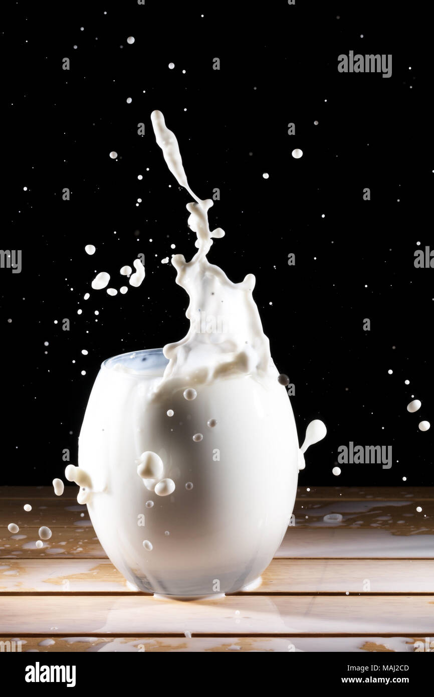 Milch/weiße Flüssigkeit splash aus Glas auf Holztisch und schwarzen Hintergrund Stockfoto