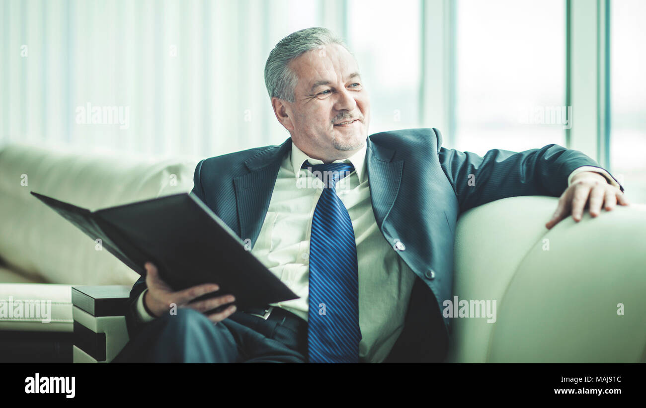 Erfolgreicher Geschäftsmann erwägt, einen neuen Vertrag auf dem Sofa sitzen im eigenen Büro Stockfoto