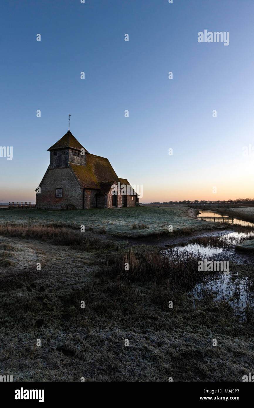 Der hl. Thomas Becket Kirche in die Sümpfe. Winter Dawn Twilight, Frost auf den Boden, halb gefrorenen Graben mit Schilf, Kirche am Horizont. Romney Marsh, Großbritannien. Stockfoto