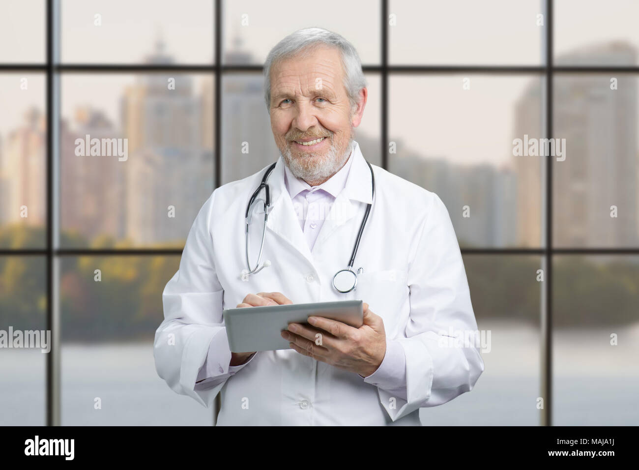 Leitender Arzt mit seinem Tablet Computer am Arbeitsplatz. Arzt mit Tablet Computer im Krankenhaus Lobby, karierte Windows Hintergrund. Stockfoto