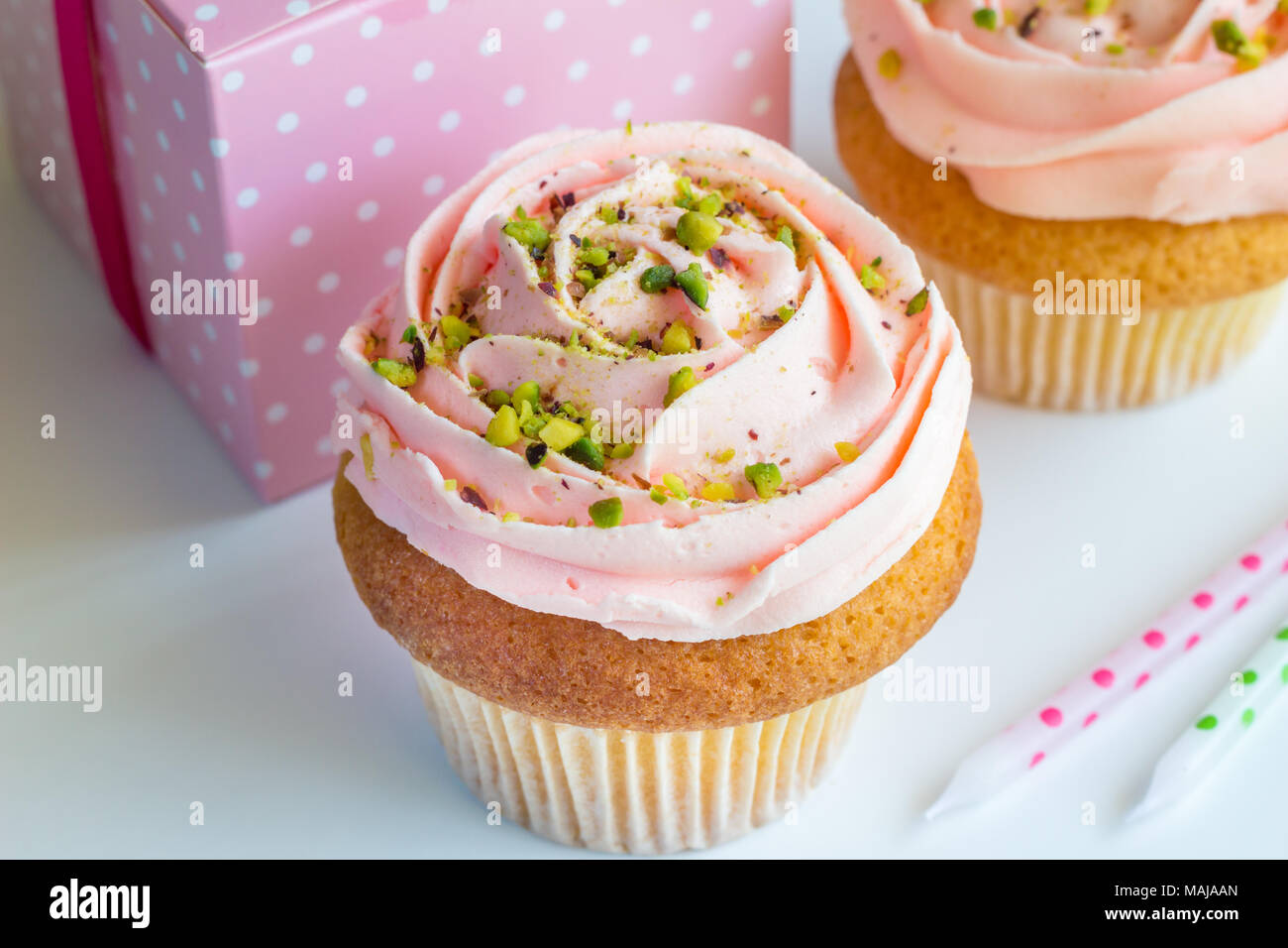Dekoriert rosa cup cakes mit Pistazie besprüht - Geburtstag Hintergrund mit Geschenk und unbeleuchteten Kerzen Stockfoto