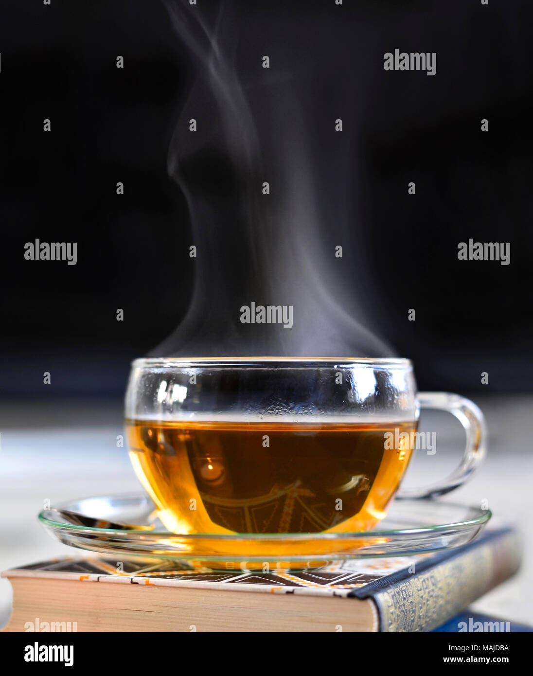 Teatime Szene mit Glas Teekanne und Tasse Tee, altes Buch und heißen Dampf. Idyllische Tea Time oder Entspannung Szene mit Plätzchen und Kerzen. Stockfoto