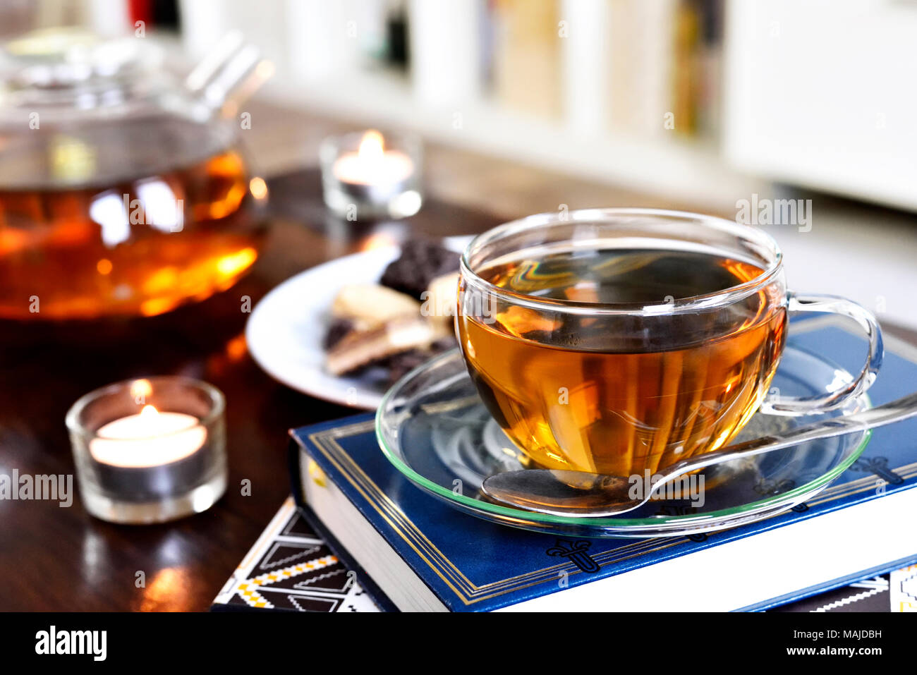 Teatime Szene mit Glas Teekanne und Tasse Tee, altes Buch und heißen Dampf. Idyllische Tea Time oder Entspannung Szene mit Plätzchen und Kerzen. Stockfoto