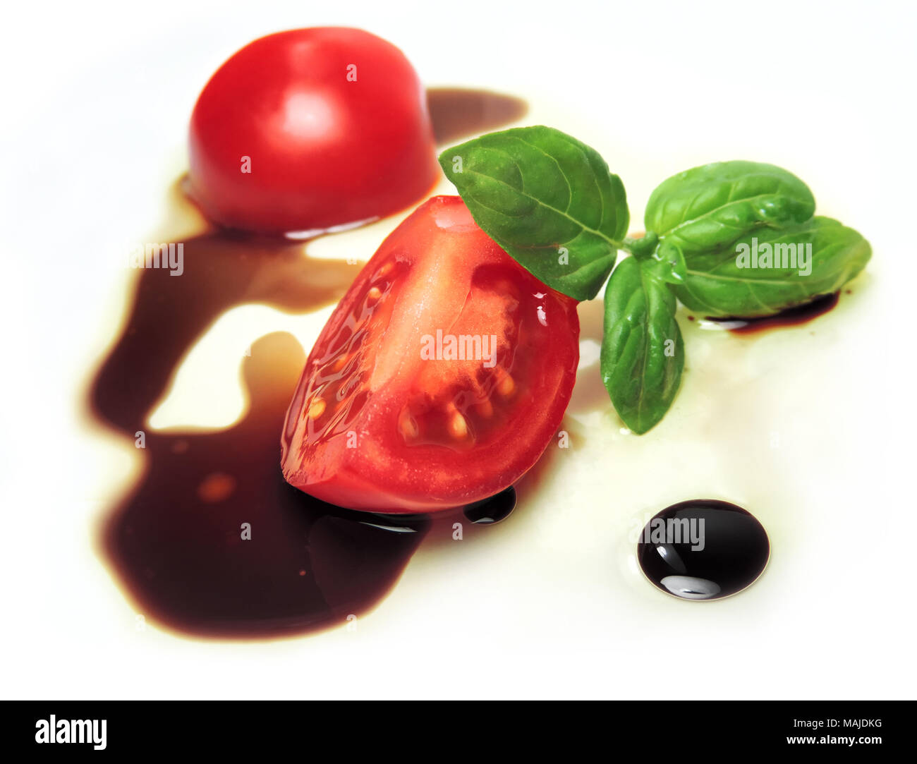 Cherry Tomaten mit Öl und Essig, auf weißem Hintergrund und mit Basilikum Blatt eingerichtet. Tomaten in Scheiben schneiden und aceito Balsamico. Italienisches Essen. Stockfoto