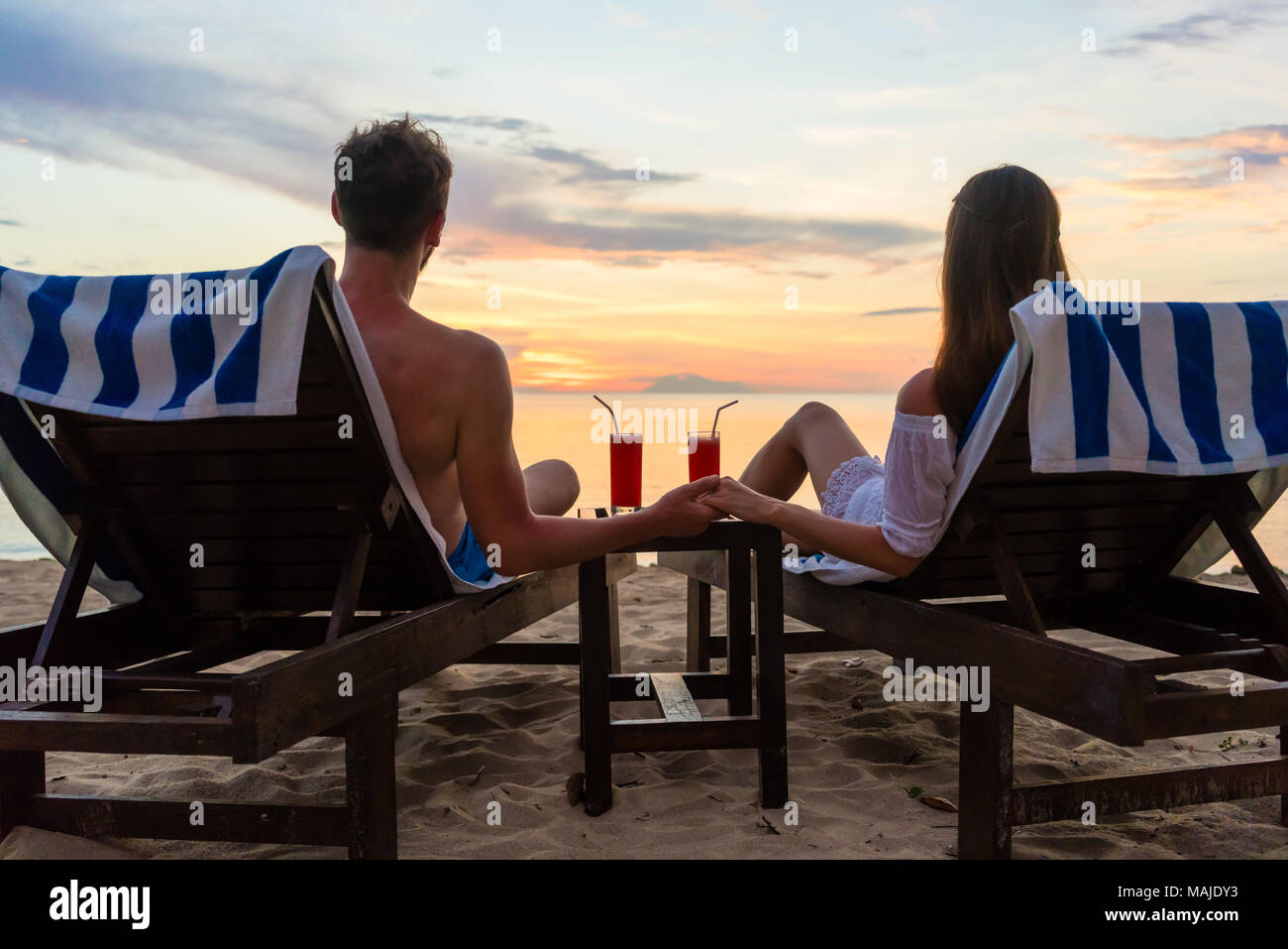 Junges Paar trinken Cocktails am Strand bei Sonnenuntergang während der Ferien Stockfoto