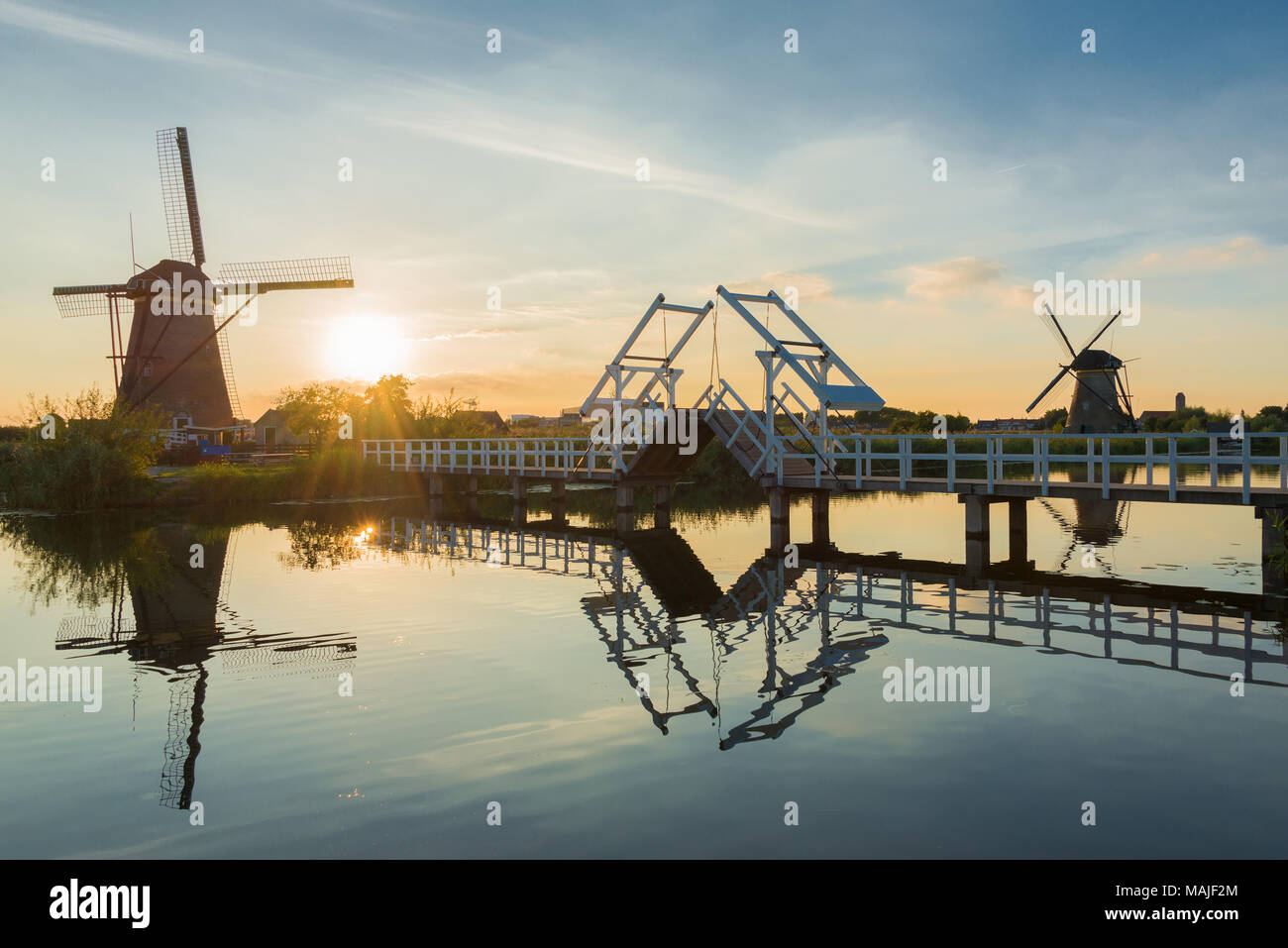 Eine Landschaft in den Niederlanden mit zwei Windmühlen und eine Zugbrücke in die niedrige Sonne bei Sonnenuntergang mit Reflexion im Wasser in Kinderdijk, Niederlande. Stockfoto