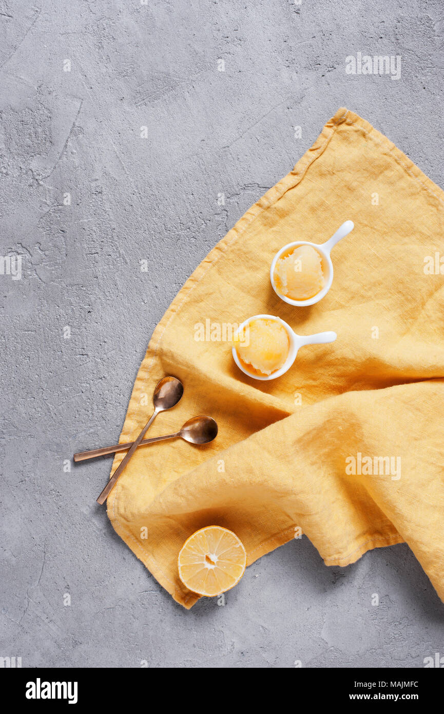 Zwei Portionen Zitronensorbet in die weiße Schüssel auf gelb serviette, strukturierte graue Tabelle. Ansicht von oben Stockfoto