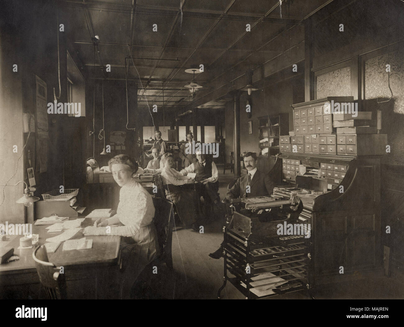 Horizontale Foto des Inneren ein Büroraum mit Männern und Frauen an der Schreibtische und ständigen Sitzen. Titel: Frauen und Männer im Amt Standard hinzufügen Machine Company, 3701 Forest Park Boulevard. . Mai 1910. Stockfoto