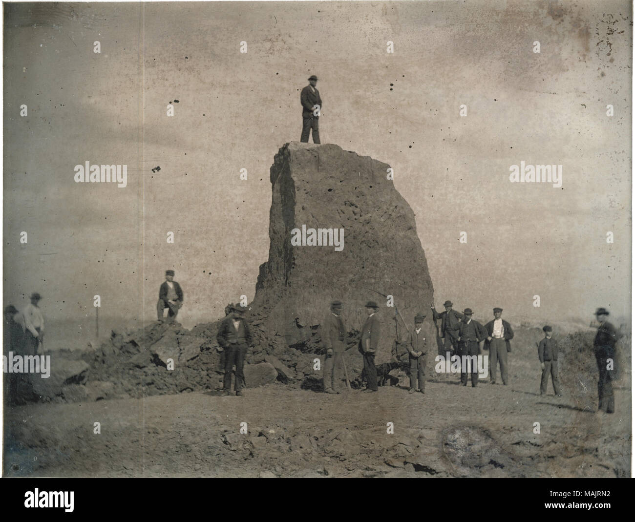 Viele Männer und einige Jungen stand auf und vor dem großen Damm während seiner Vernichtung. Dies ist der letzte der großen Damm; nur ein kleiner Teil bleibt stehen. Ein Junge hält eine Spitzhacke, der in den Hügel gestellt wird. Titel: Große Damm während der Zerstörung, der letzte der großen Damm. . 1869. Thomas M. östlich Stockfoto