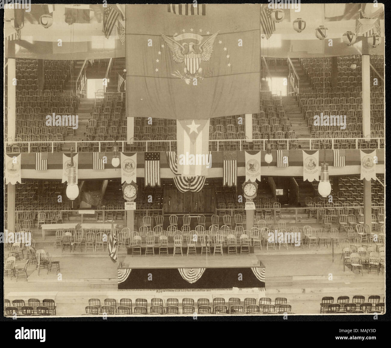 Horizontale, sepia Foto, ein Podium und leere Stühle aus Holz auf dem Boden, hinter dem Podium und in den Balkon über dem Podium. Flaggen und Fahnen hängen von den Balkon und Decke. Titel: Innenansicht des Podium in der "Wigwam" an der Republican Convention Hall, 1896. . 1896. Emil Boehl (zugeschrieben) Stockfoto