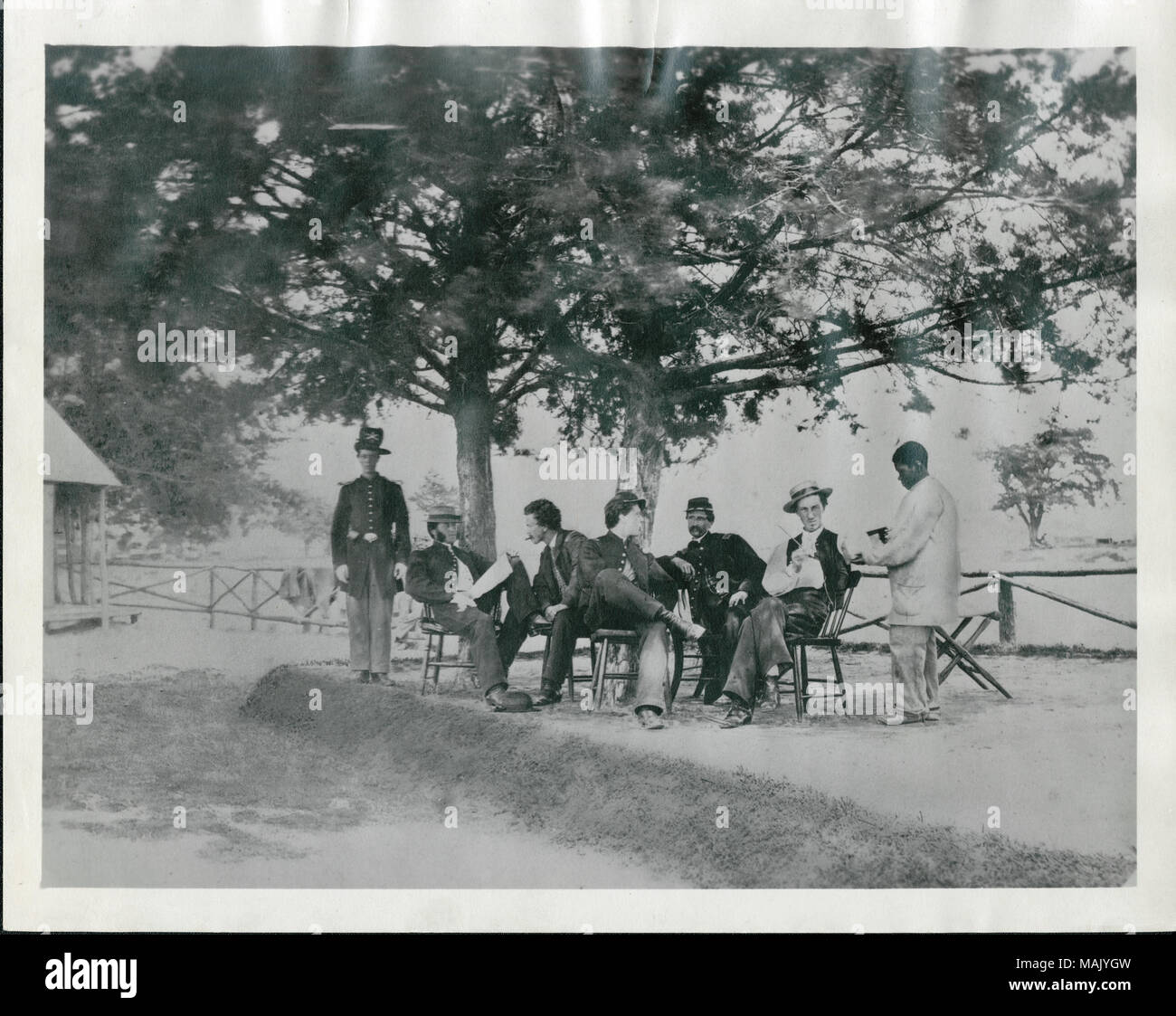 Gruppenfoto von fünf Männern, die Union Offiziere zu werden, eine Union eingetragenen Mann (wahrscheinlich ein eigenes), sowie eine Afrikanische amerikanische Diener. Die Männer sind unter zwei Bäumen und vor einem Zaun. Im Hintergrund ist die Ecke eines Gebäudes. Die ausgehuniform Mann hat eine Hardee Hut auf mit dem, was entweder gekreuzt Kanonen oder Säbel und einem Unternehmen schreiben. Titel: Nicht identifizierte Offiziere mit African American Attendant (Union). . Zwischen 1861 und 1865. Stockfoto