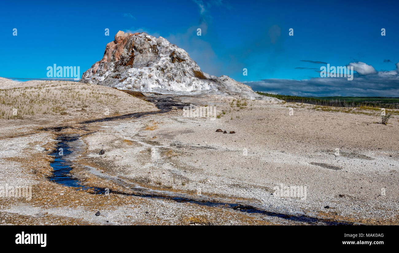 Geysir Damm mit einer kleinen Menge Dampf auf einem unfruchtbaren wastland mit kleinen Strom von Wasser läuft aus Damm gegen einen blauen Himmel. Stockfoto