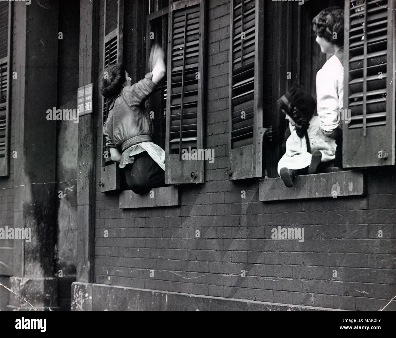 Horizontal, schwarz-weiß Foto von zwei Frauen und ein Baby in die Fenster eines Gebäudes. Die Frau auf der linken wäscht die Außenseite der Fenster wie die anderen an schaut. Titel: Waschmaschine Windows in einem St. Louis Wohnung. Das Haus bot "möblierte Zimmer" zu "Herren." um 1910. Stockfoto