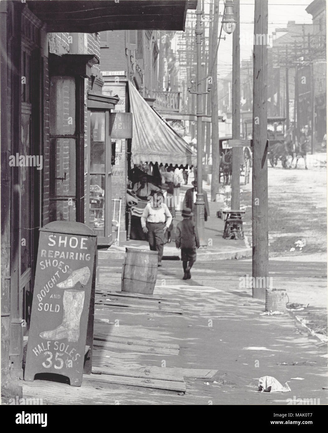 Titel: Bürgersteig Szene auf einem nicht identifizierten Straße. Schuhreparatur Schild in der linken Hälfte Sohlen 35 (Cent). . Ca. 1900. Stockfoto