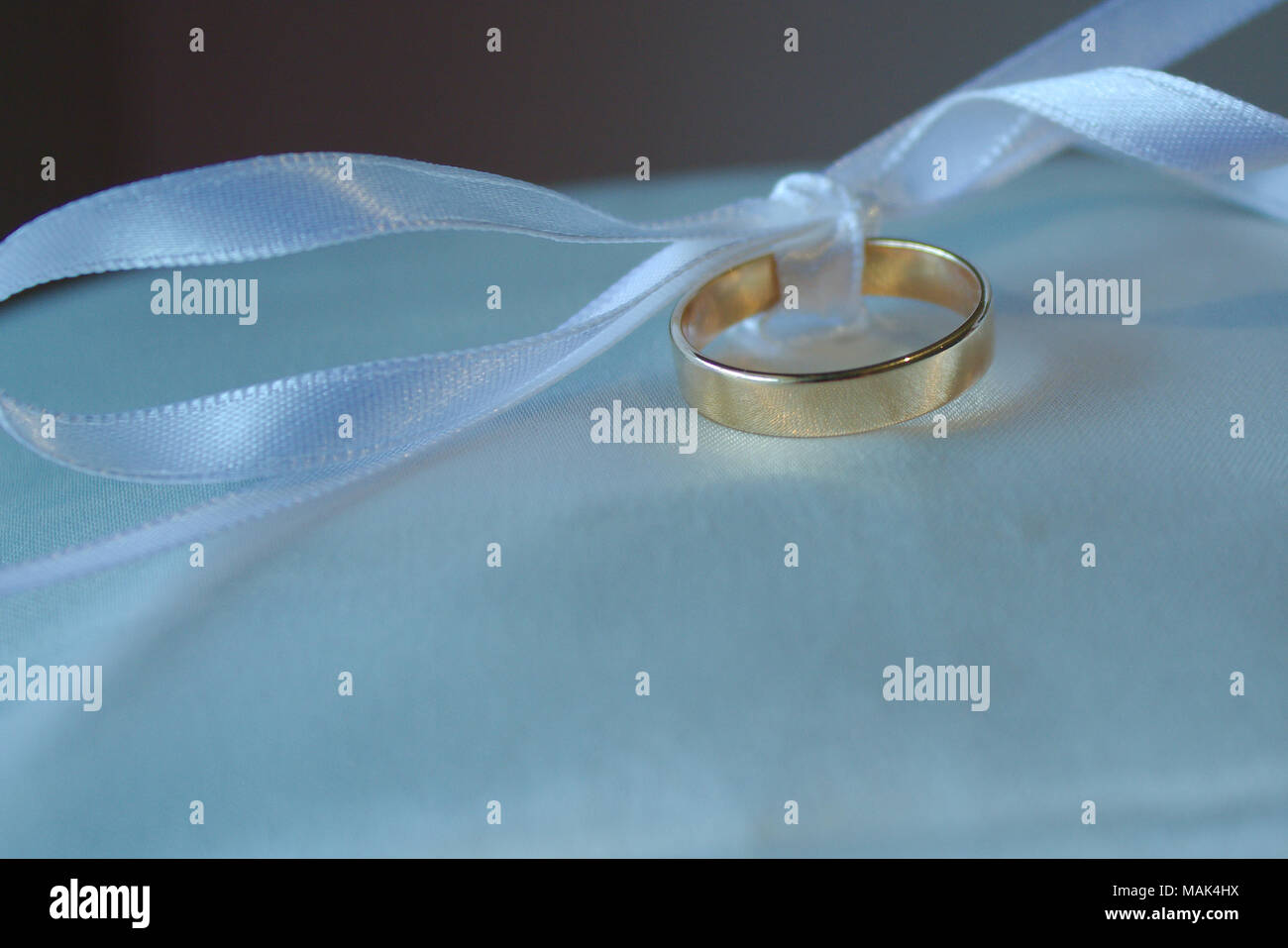 Eine weiße Schleife in einer Schleife gebunden hält einen Ehering auf einem Kissen. Stockfoto