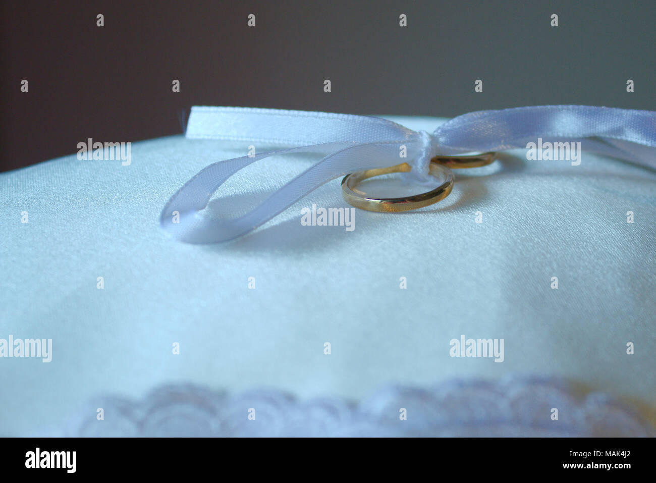 Eine weiße Schleife in einer Schleife gebunden hält Hochzeit Ringe auf einem Kissen. Stockfoto